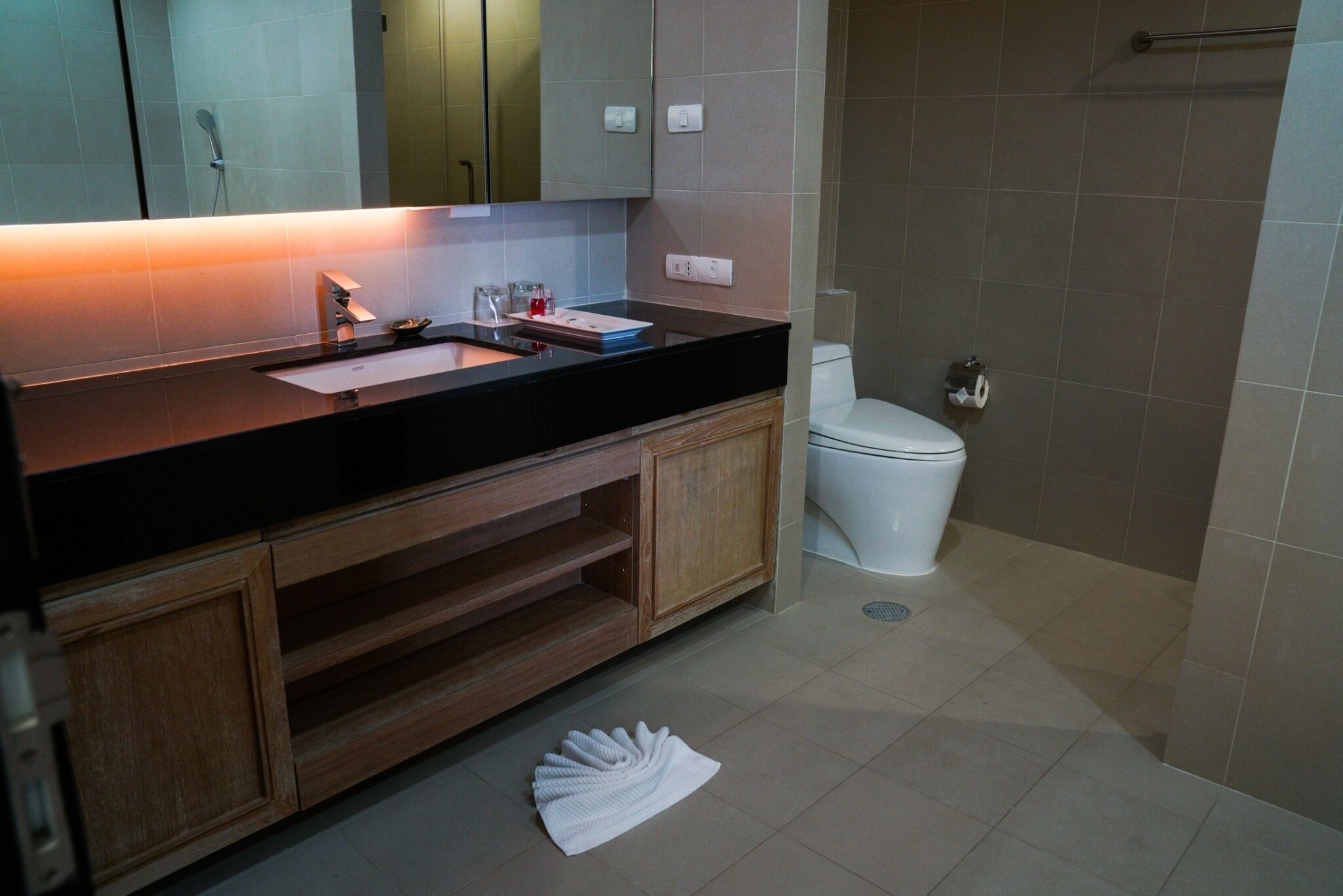 Un baño moderno con encimera negra, armarios de madera, inodoro blanco y zona de ducha.