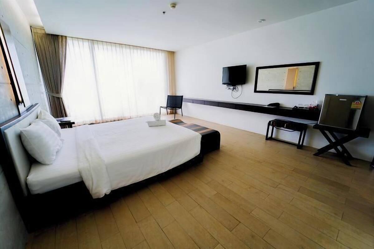 A hotel room with a large bed, a desk, a chair, a TV, and a mirror.