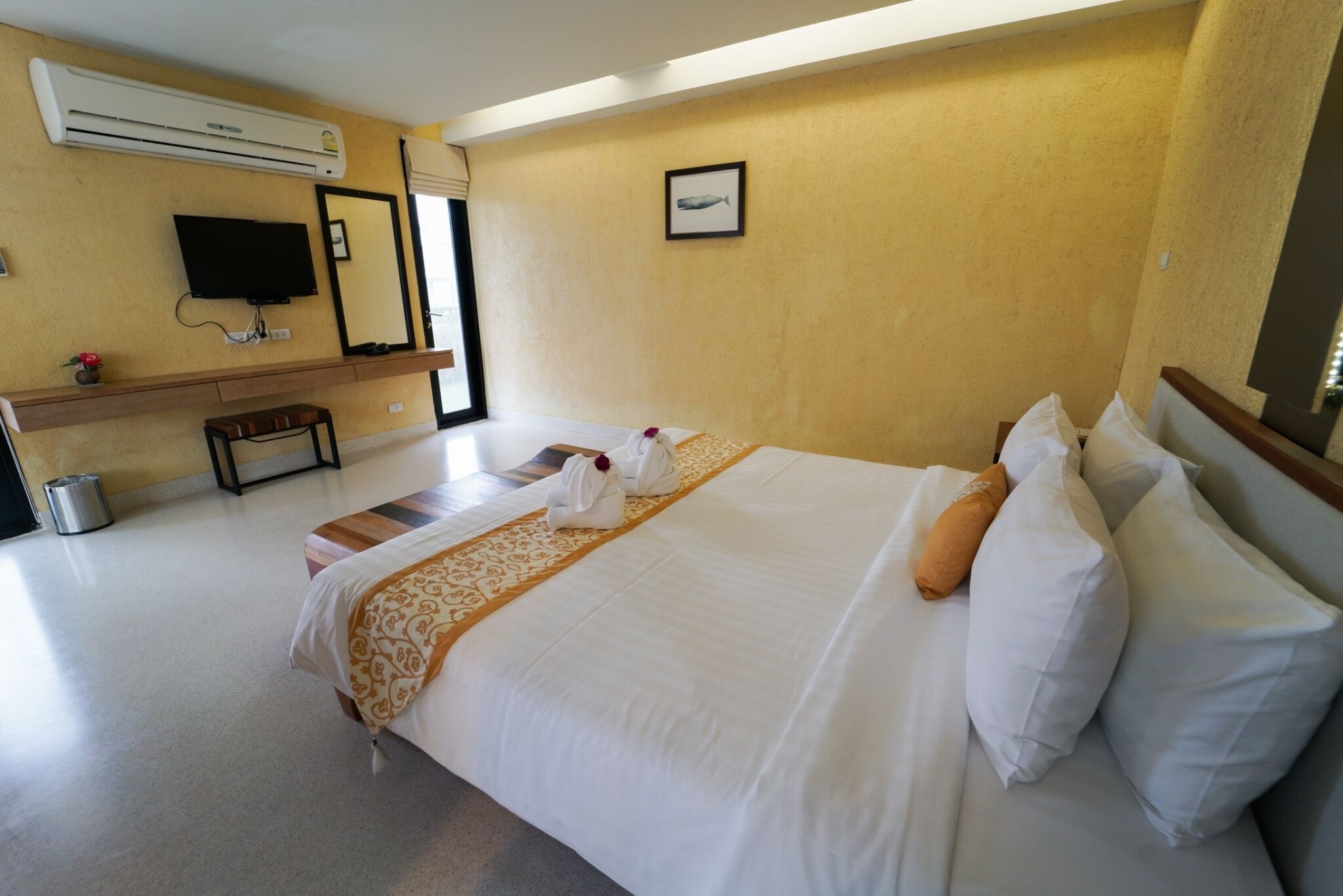 A hotel room with a large bed, a flat-screen TV, an air conditioning unit, a small table, and a trash bin.