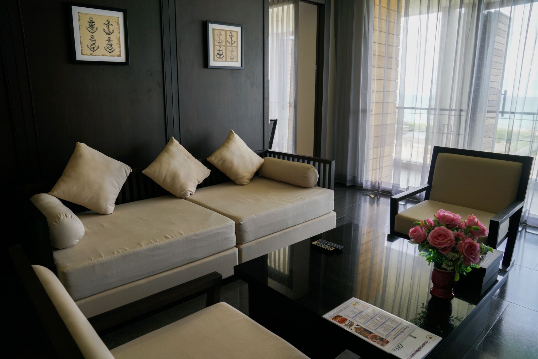 Une chambre d’hôtel moderne avec un canapé, des fauteuils, une table basse en verre et un vase de fleurs.