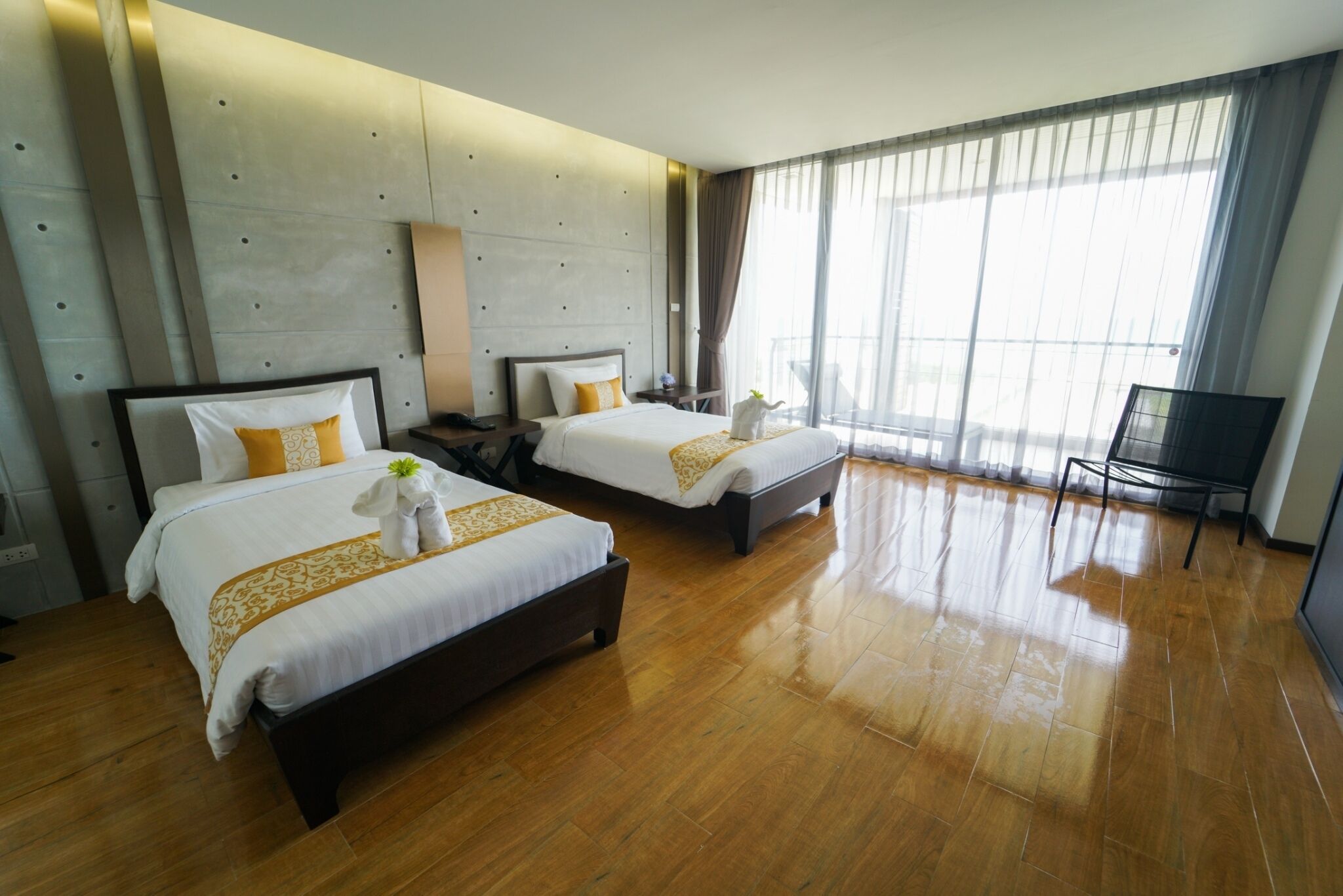 Habitación de hotel con dos camas, un ventanal con cortinas, suelo de madera y una televisión.