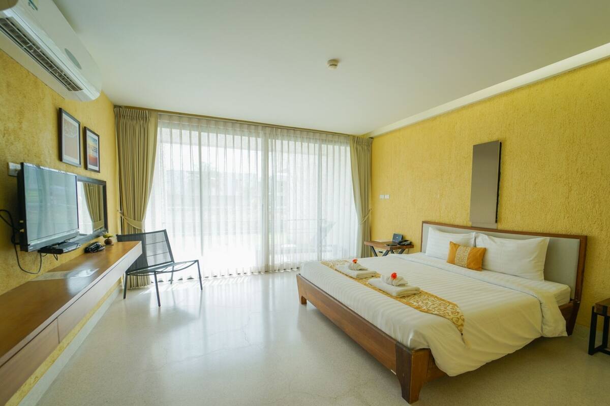 A hotel room with a bed, a desk with a TV, a chair, and a large window with curtains.
