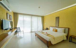 Habitación de hotel con cama, escritorio con televisor, silla y ventana grande con cortinas.