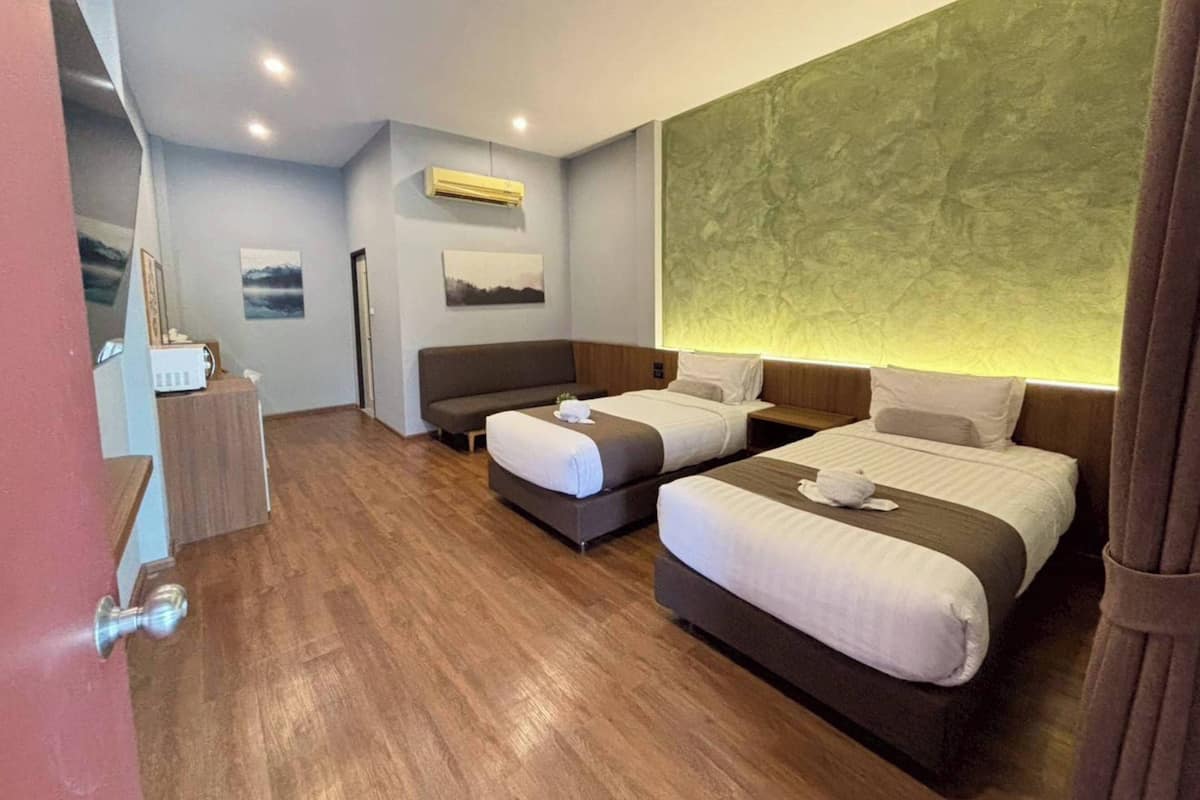 Ein Hotelzimmer mit zwei Betten, Holzboden, Klimaanlage und einer Wand mit grüner Struktur.