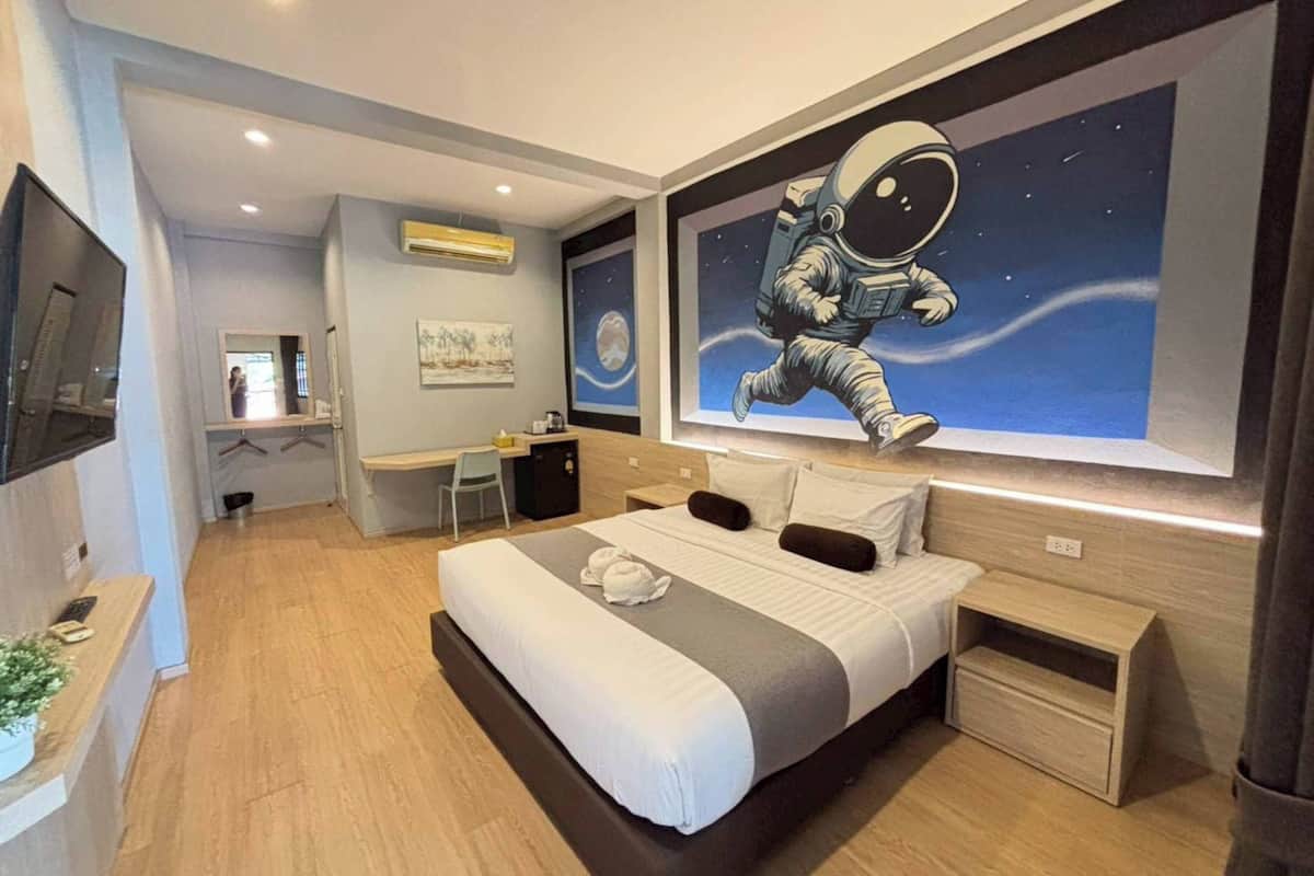 Ein modernes Hotelzimmer mit einem großen Bett, einem Schreibtisch, einem Stuhl, einer kleinen Kommode und einem an der Wand befestigten Fernseher.