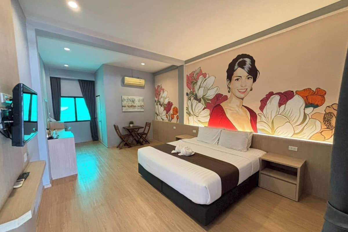 Ein Hotelzimmer mit Bett, Nachttisch, Fernseher, Schreibtisch, Sessel und einer großen Blumenmalerei an der Wand.