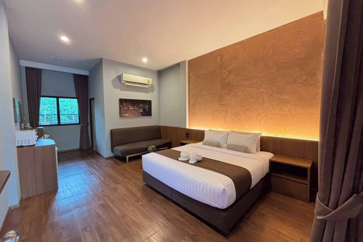 Ein Hotelzimmer mit Bett, Nachttischen, einer Couch, einem Fenster, einer Klimaanlage und einem Wandbild.