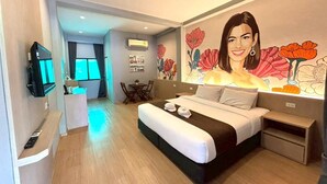 Een hotelkamer met een bed, een televisie, een eethoek en een muurschildering.