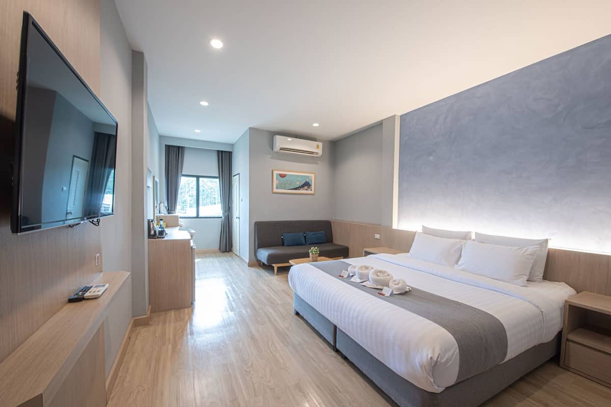 Ein modernes Hotelzimmer mit einem großen Bett, einem Flachbildfernseher, einer Couch, einem Schreibtisch mit Lampe und einer Klimaanlage.