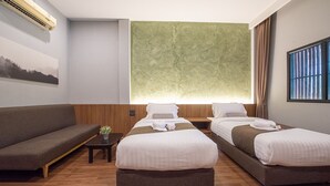 Een hotelkamer met twee bedden, een bank, een kleintje tafeltje met een plant en een groot raam met gordijnen.