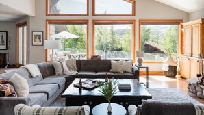A spacious living room with a large sectional sofa, a coffee table, and a view of a mountainous landscape through large windows.