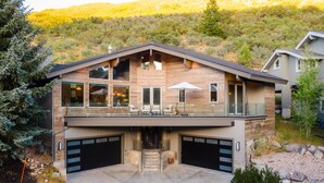 A modern two-story house with a large deck, multiple garage doors, and a swimming pool in the foreground.