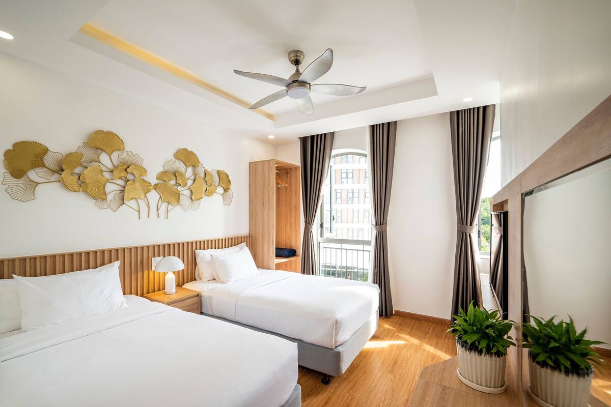 Une chambre d’hôtel avec deux lits, un ventilateur de plafond, une grande fenêtre avec des rideaux et un élément décoratif fixé au mur.
