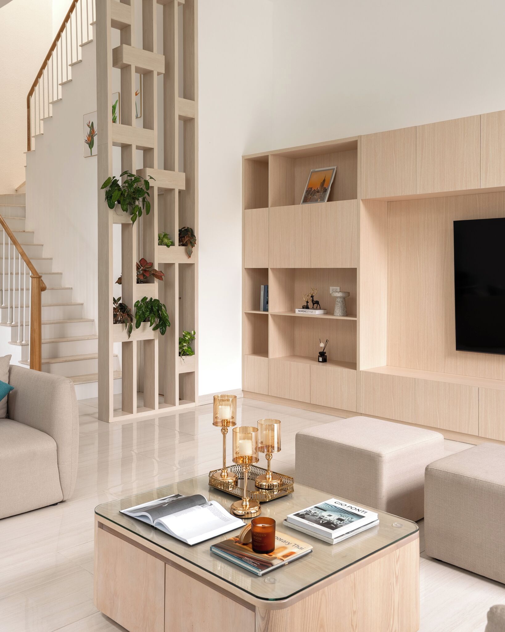 A modern living room with a glass coffee table, a sofa, a TV mounted on the wall, and a staircase with a wooden railing.