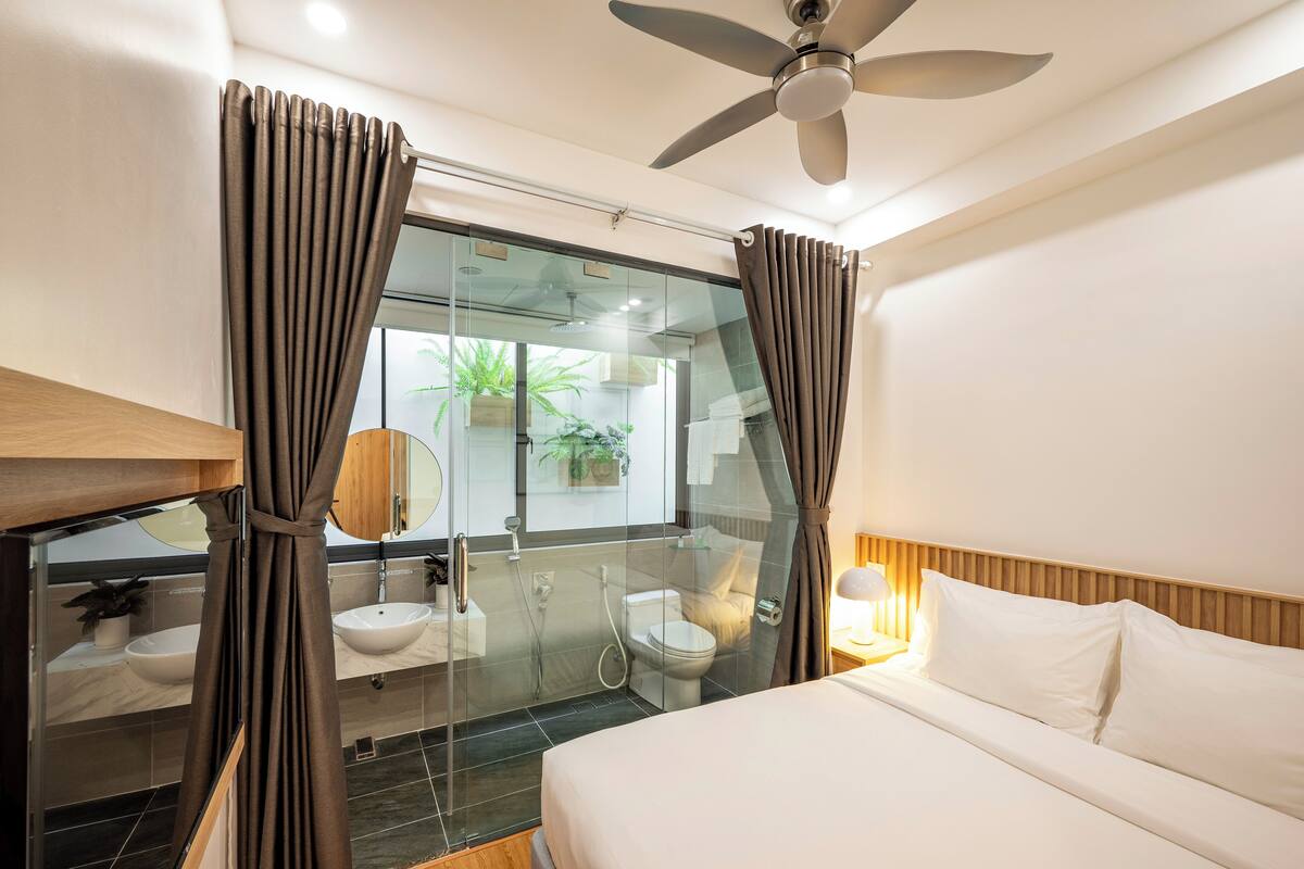 Une chambre d’hôtel moderne équipée d’un lit, d’une table de chevet et d’une douche séparée par des parois en verre.
