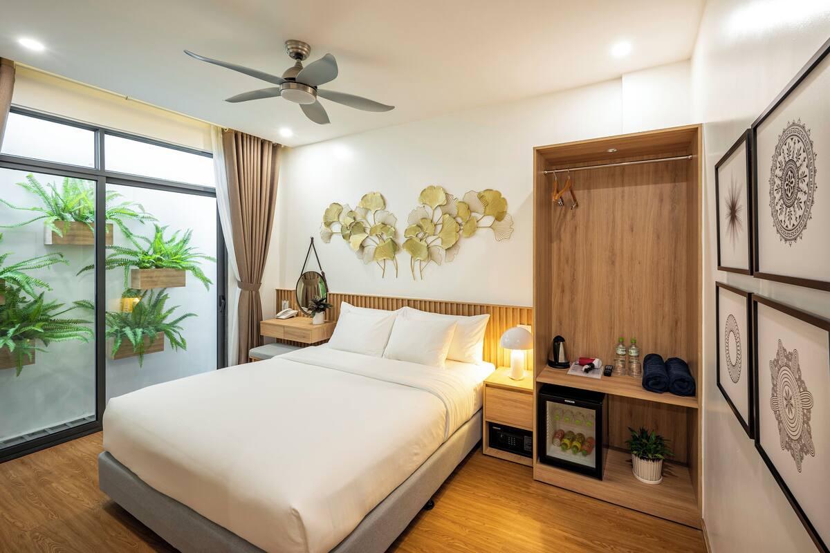 Une chambre d’hôtel moderne dotée d’un grand lit, d’un ventilateur de plafond, d’une table de chevet avec une lampe, d’une armoire en bois et d’œuvres d’art décoratives murales.