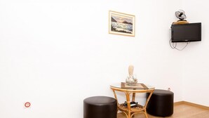 A minimalist room with a glass-top table, two black stools, a wall-mounted TV, and a framed painting. - Villa Barbara (Zupa dubrovacka)