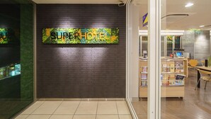 A hotel reception area with a dark brick wall and a sign that reads "SUPERHOTEL". - Super Hotel Midousuji Line Esaka (Suita)