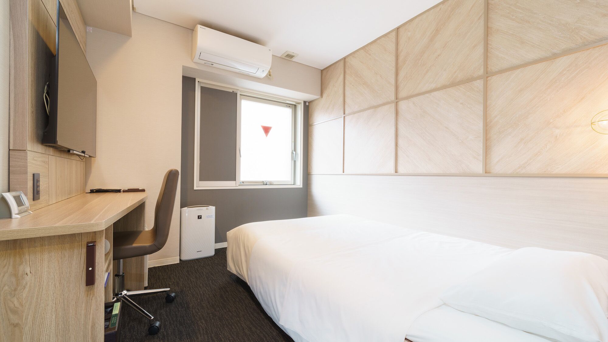 A hotel room with a bed, a desk with a chair, a TV, a window with a view, and an air conditioning unit.