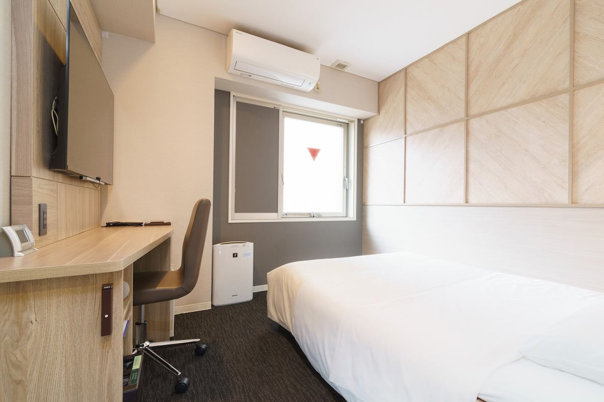 Hotelkamer met een bed, bureau met stoel, televisie, raam met uitzicht en een airconditioning.