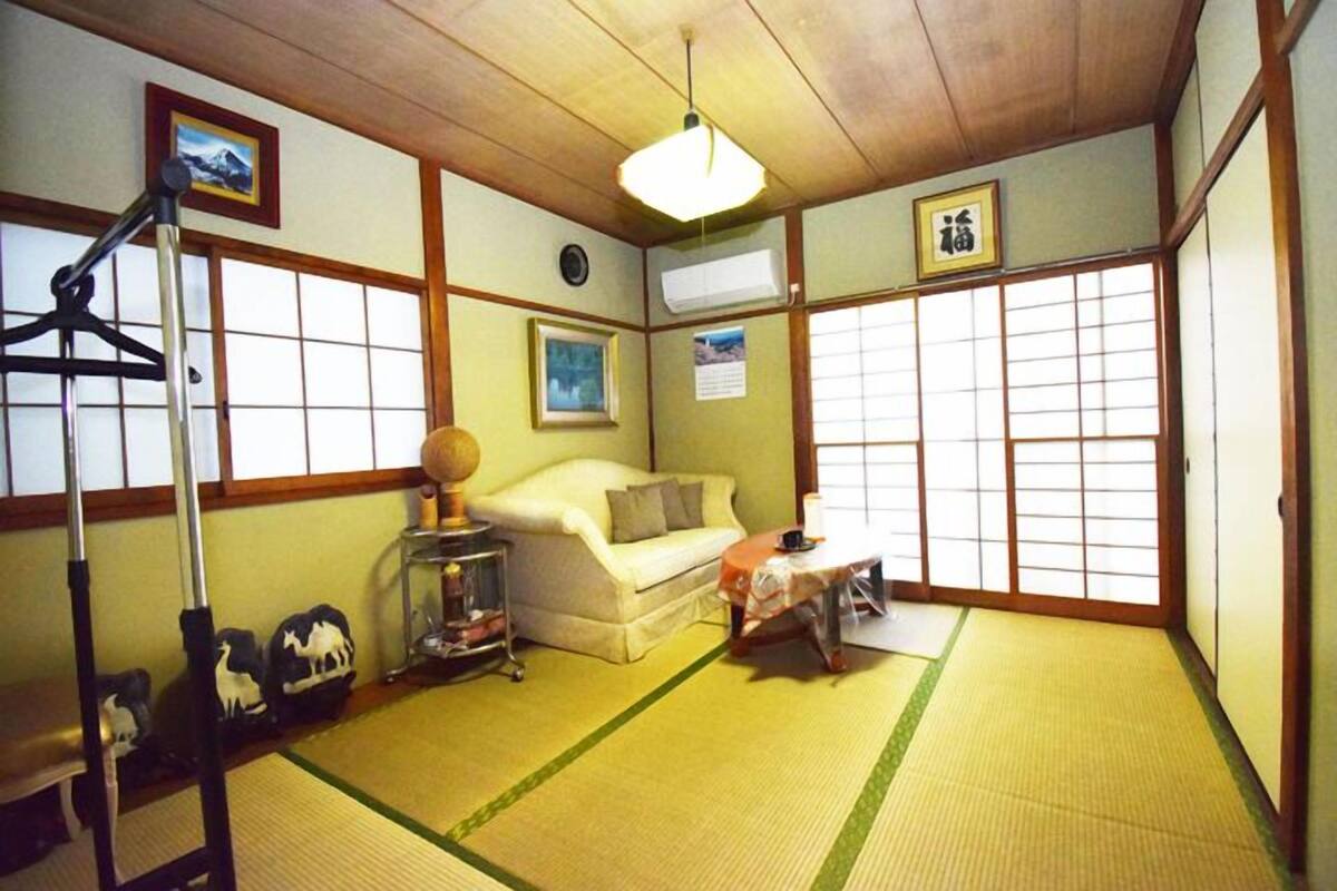 A traditional Japanese room with tatami flooring, a sofa, a small table, and a hanging lamp.