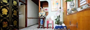 A traditional Japanese room with tatami flooring, a shoji screen, a wooden cabinet with decorative items, and a small table with a vase and a statue. - Oasis Minamiyukigaya (Tokyo)