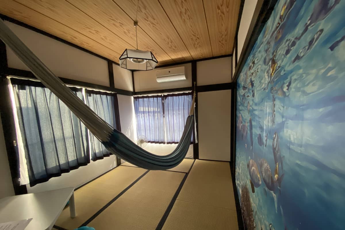 Una habitación con una hamaca, suelo de tatami, una mesa blanca y una pared grande con un acuario.