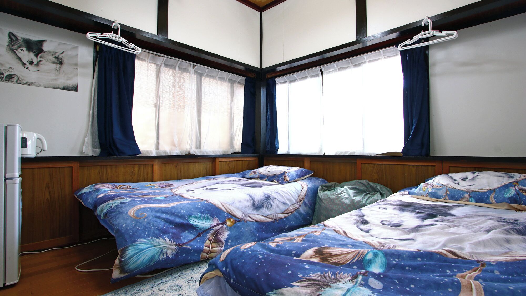 Quarto com duas camas, um refrigerador e janela com cortinas.