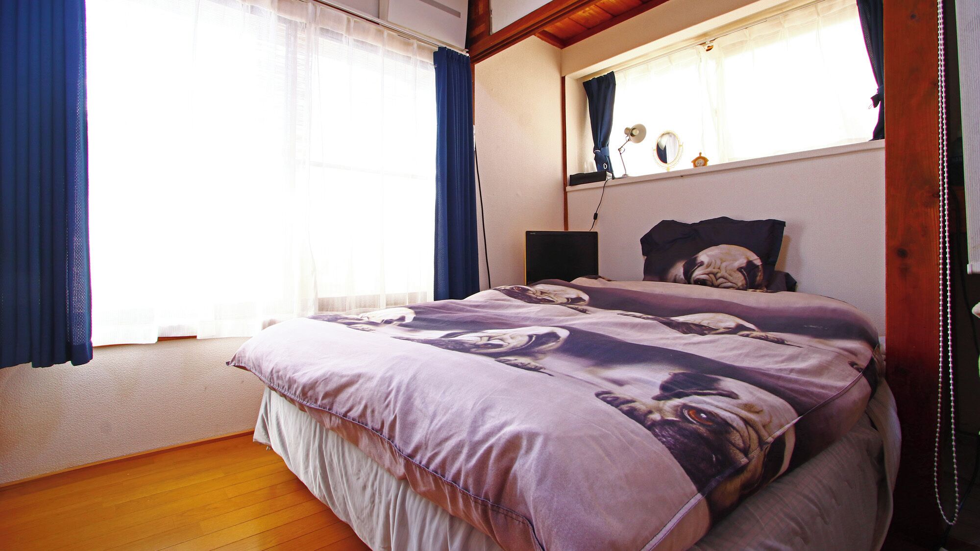 Um quarto com cama, janela com cortinas, mesa de cabeceira e luminária.