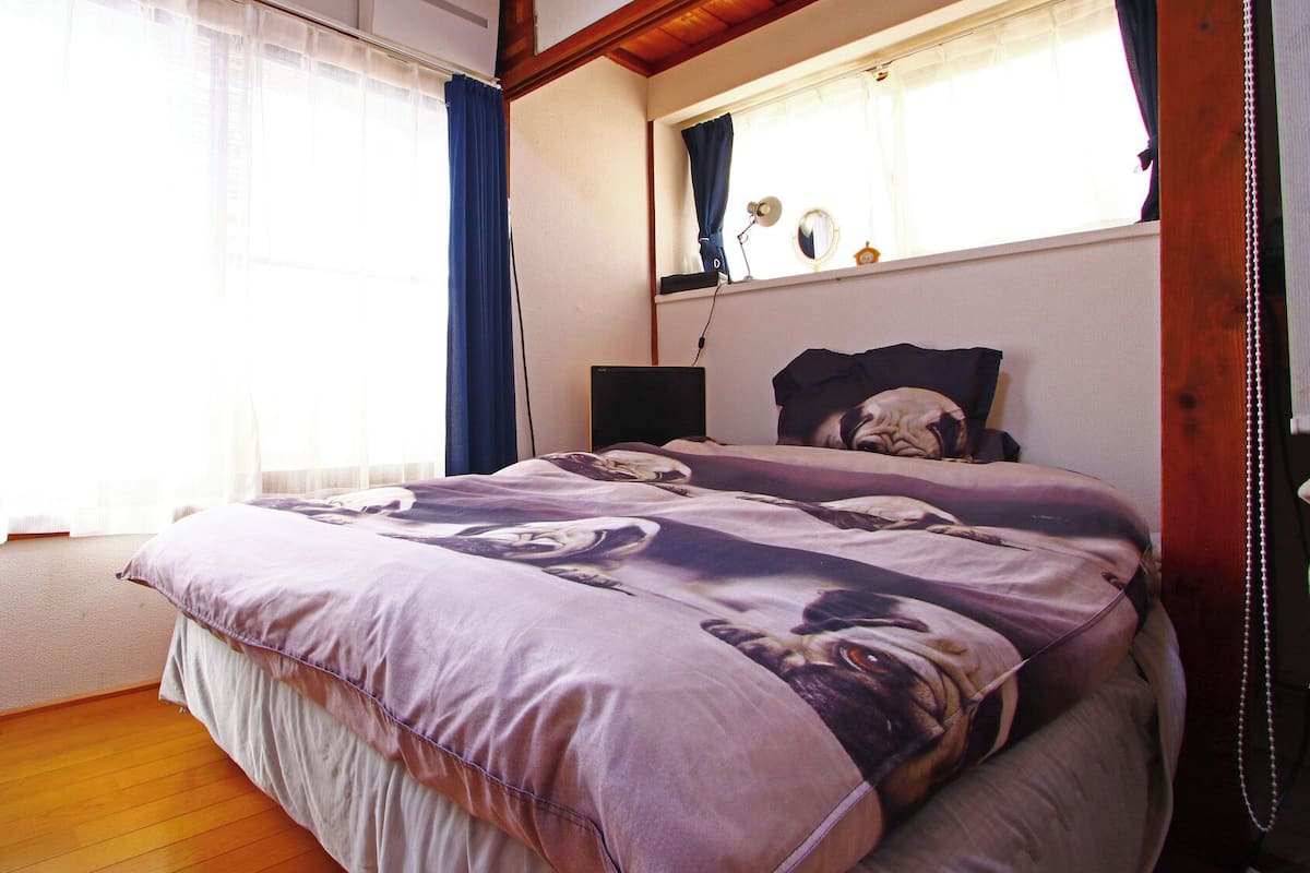 Un dormitorio con cama, una ventana con cortinas, una mesita de noche y una lámpara.