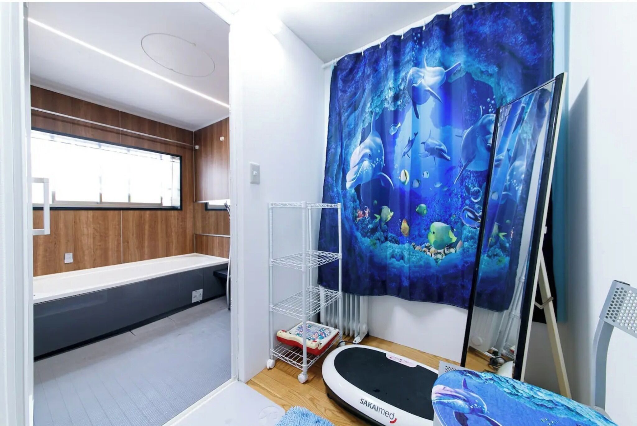 A room with a bed, a white shelf, a white chair, a white table, and a blue curtain with an underwater scene.