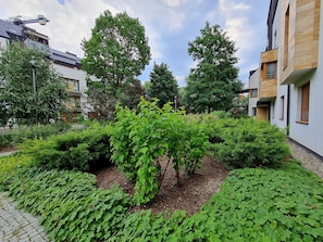 A courtyard with a variety of green plants and trees, a paved walkway, and modern buildings with balconies. - RS2.29 - Sienkiewicz Residence (RS1, RS2) (Swinoujscie)