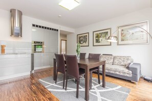A modern living room with a dining area, a sofa, and a kitchen with white cabinets and a built-in oven.