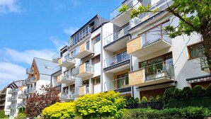 En flere-etagers boligbygning med altaner, et grønt parkområde og en klar himmel.