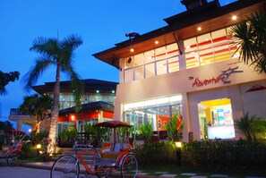 A modern hotel with a large glass facade, a visible entrance, and a bicycle parked outside. - The Adventure Hotel (Chiang Mai)