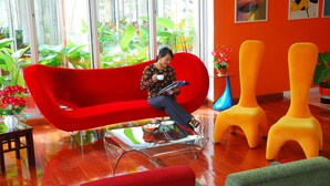 Um interior moderno com um sofá vermelho, uma mesa de centro de vidro e cadeiras vibrantes em laranja e verde.