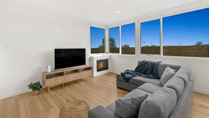 Una sala de estar moderna con un televisor de pantalla plana, una chimenea y un ventanal con vistas al campo.