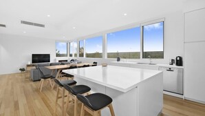 Cocina moderna con una isla grande, taburetes de bar, zona de comedor y ventanas amplias que ofrecen vistas.