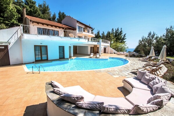 En modern villa med pool, solstolar och utsikt över havet.