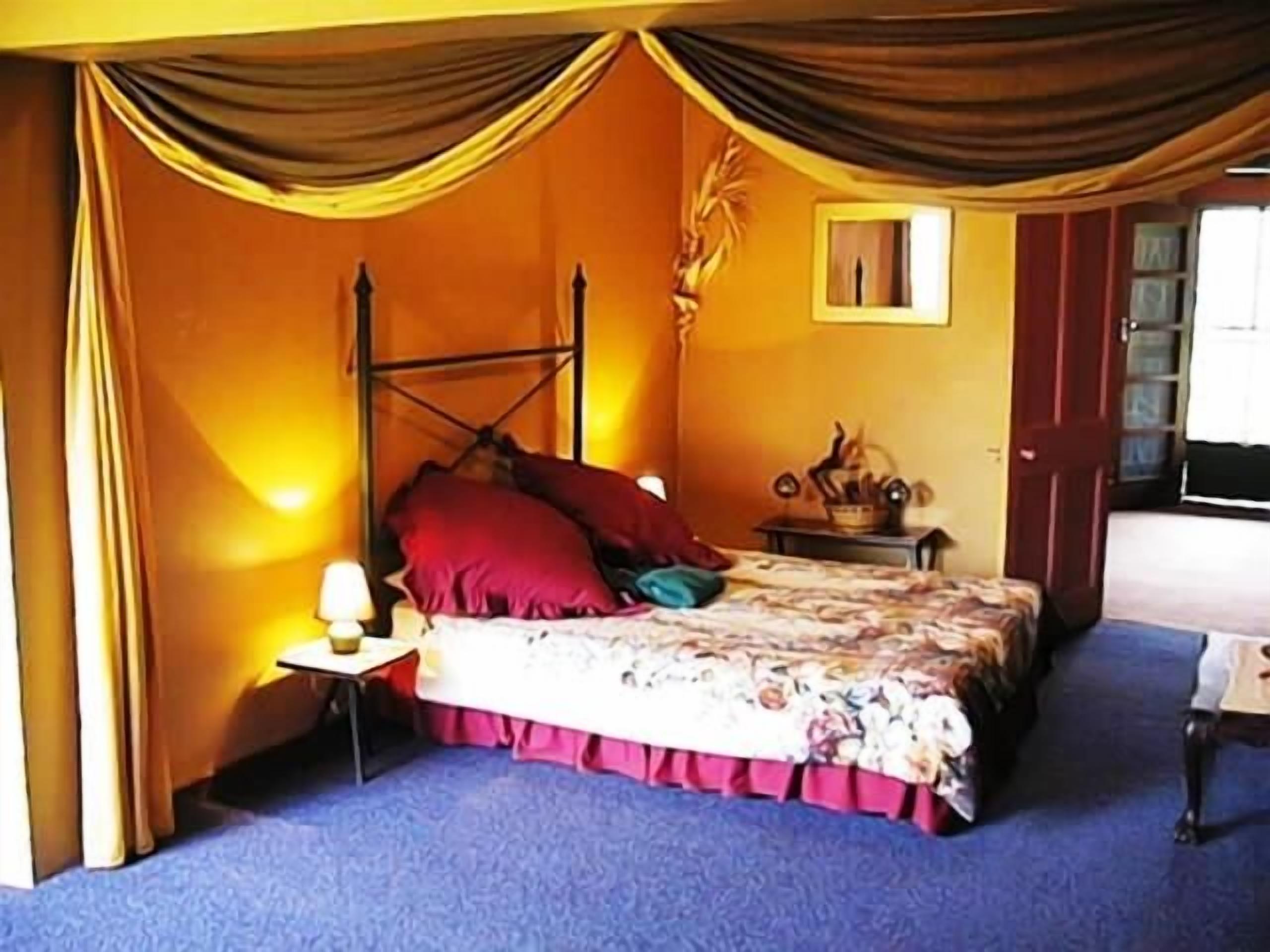 Une chambre à coucher avec un lit à baldaquin, une table de chevet, une lampe et une petite table ornée d’objets décoratifs.