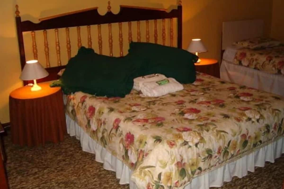 A hotel room with a floral bedspread, two bedside lamps, a wooden headboard, and a neatly made bed with a green pillow and white towels.