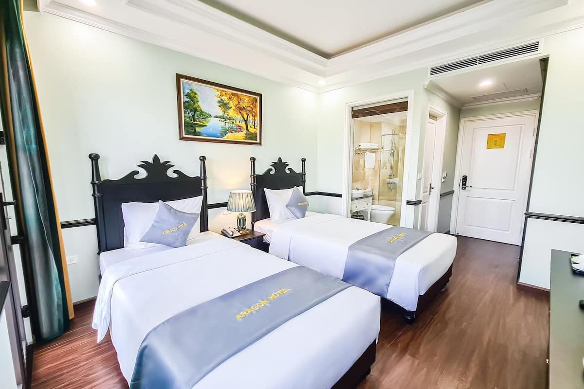 Habitación de hotel con dos camas, un cuadro en la pared y un baño visible a través de una puerta abierta.