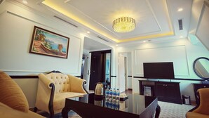 A modern living room with a chandelier, a painting, a television, and a coffee table with water bottles. - Dragon Hotel (Bai Chay)