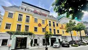 A hotel with a yellow facade, a dragon emblem, and a statue of an angel at the entrance. - Dragon Hotel (Bai Chay)