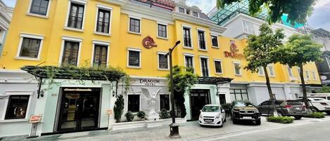 A hotel with a yellow facade, a dragon emblem, and a statue of an angel at the entrance.
