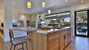 A modern kitchen with a central island, wooden cabinets, and pendant lighting.