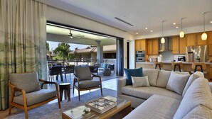 A modern living room with a sofa, chairs, and a coffee table. There is a balcony with outdoor furniture and a view of the outside.