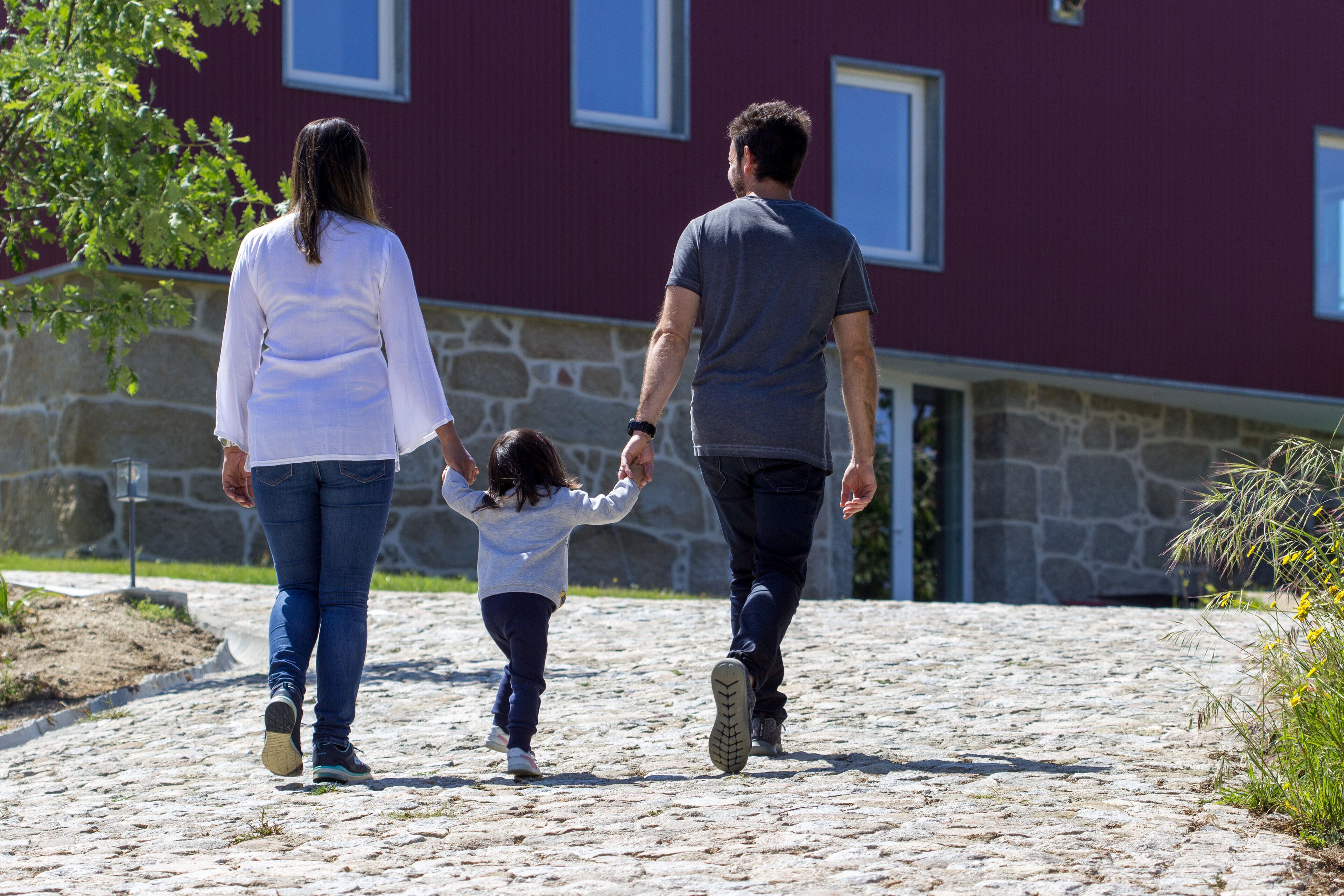 A family walking on a cobblestone path in front of a building with stone walls and windows.