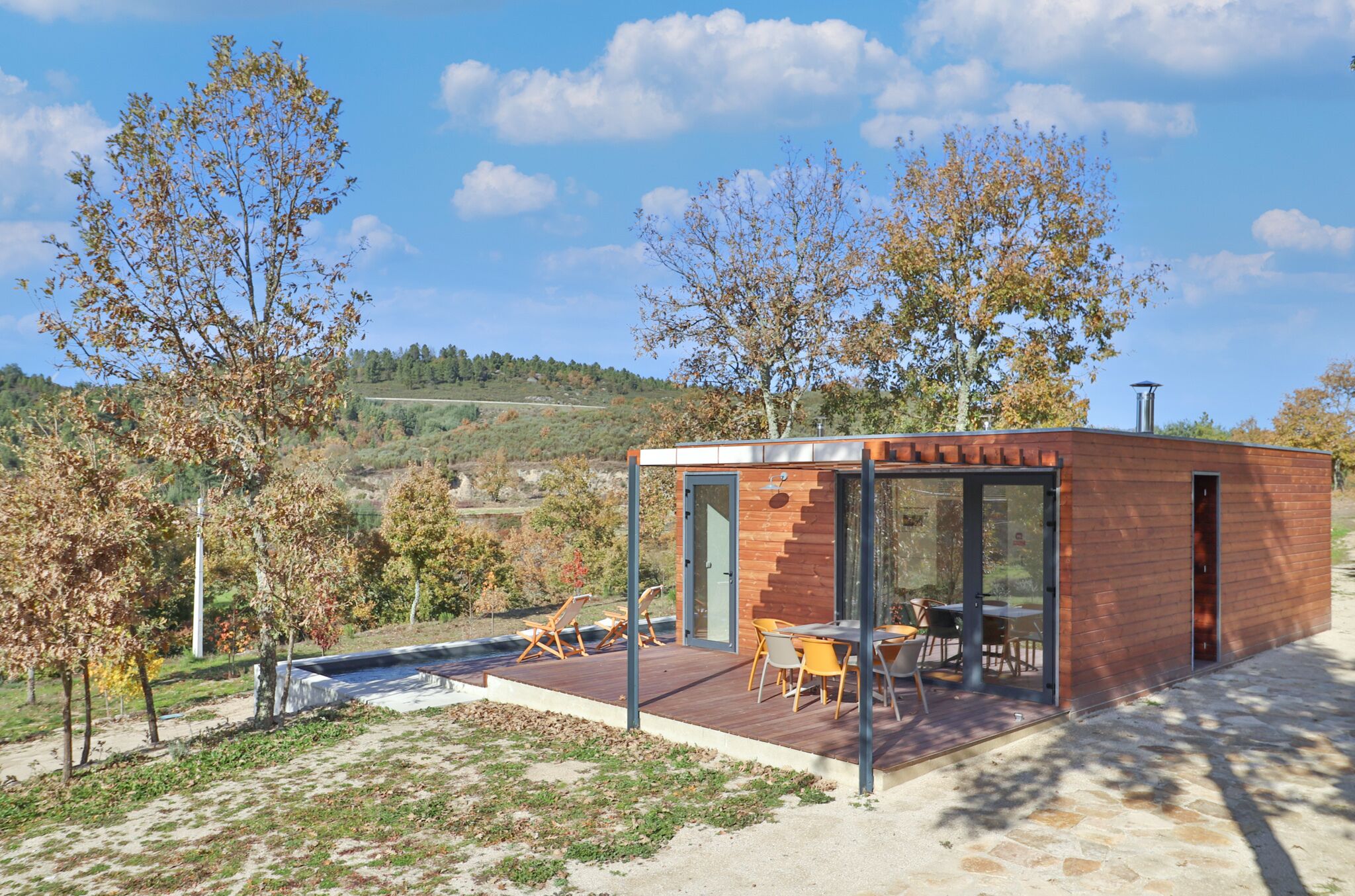 Ein modernes Haus mit Glastür, Holzterrasse und Gartenmöbeln.