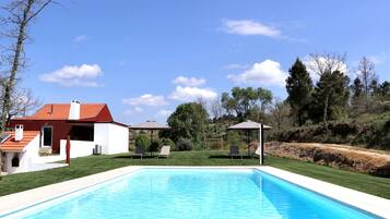 A swimming pool with lounge chairs and a gazebo, surrounded by a house and trees.